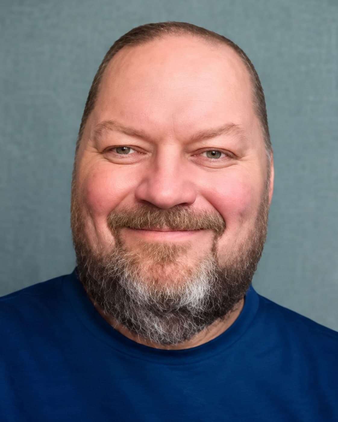 David Copeland, smiling, with close-cropped hair and a graying beard, in a navy T-shirt